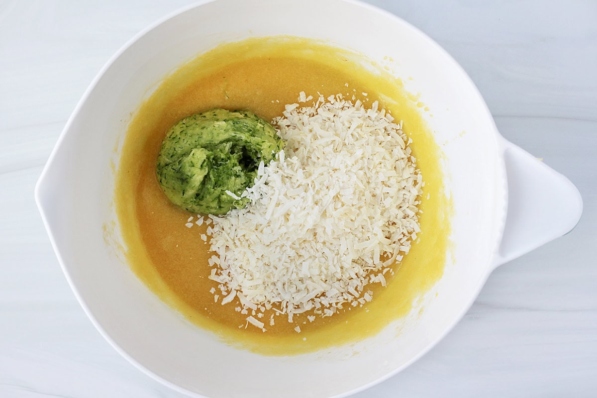 Shredded zucchini with the water squeezed out and shredded coconut in a bowl of batter.