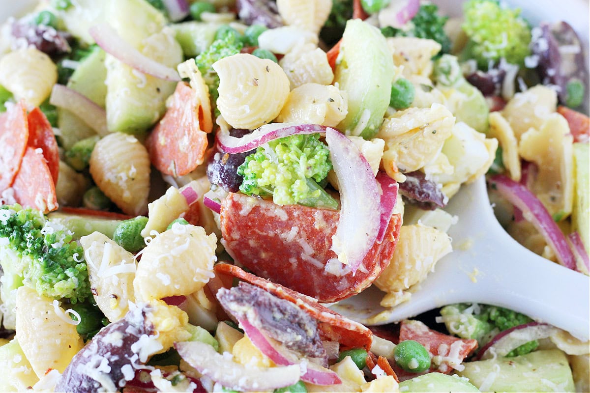 Up close photo of a white silicone serving spoon digging into loaded veggie pasta salad.