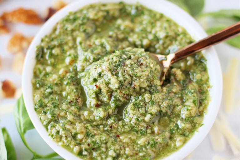 Up close photo of easy basil walnut pesto in a white bowl with a spoon.