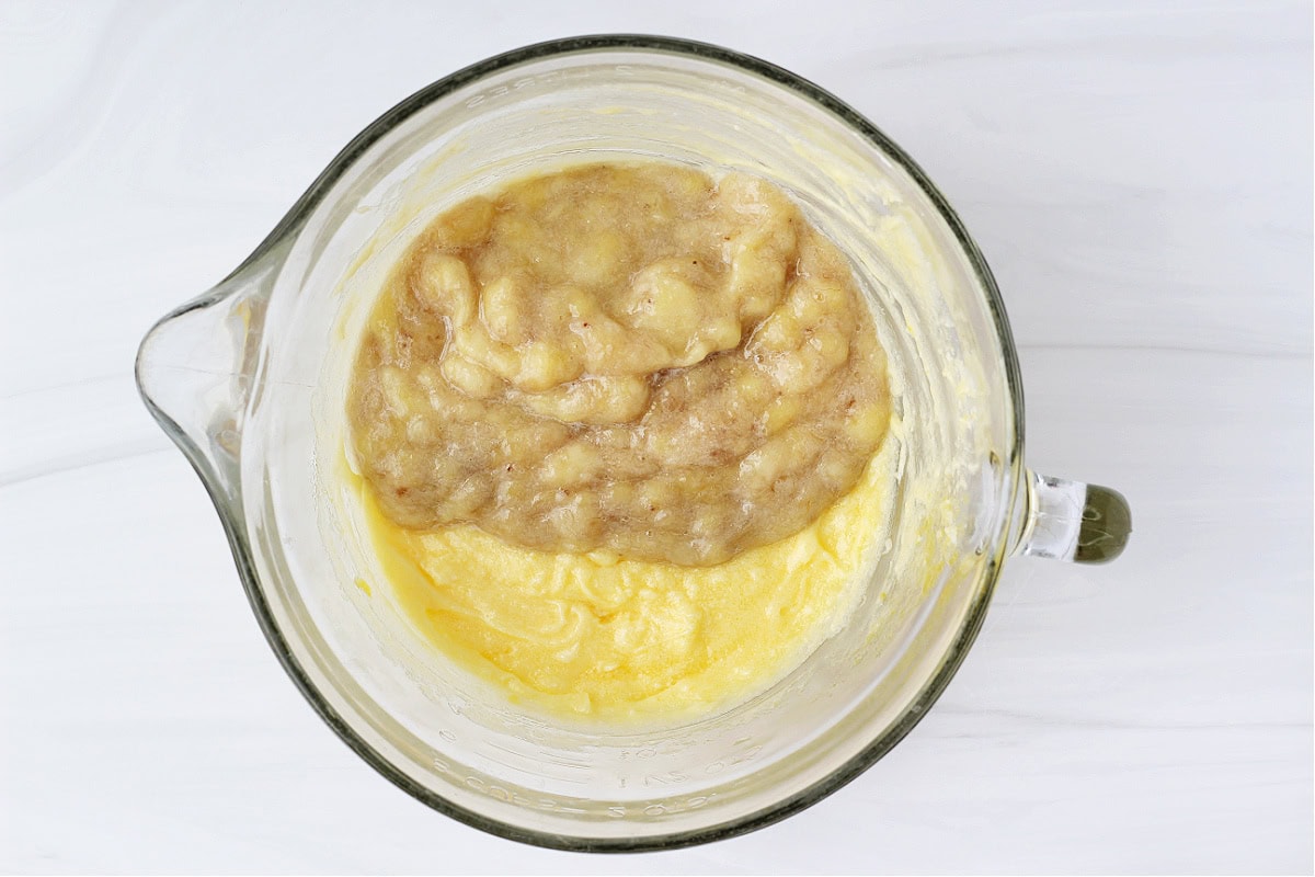 Overhead photo of mashed bananas on top of wet ingredients in a glass bowl.