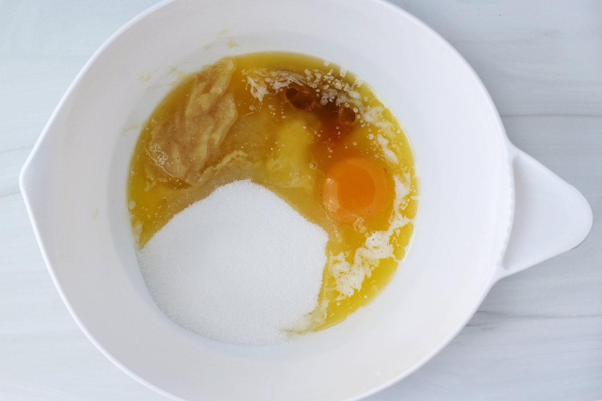 Sugar, eggs, vanilla extract, applesauce and melted butter in a white mixing bowl.