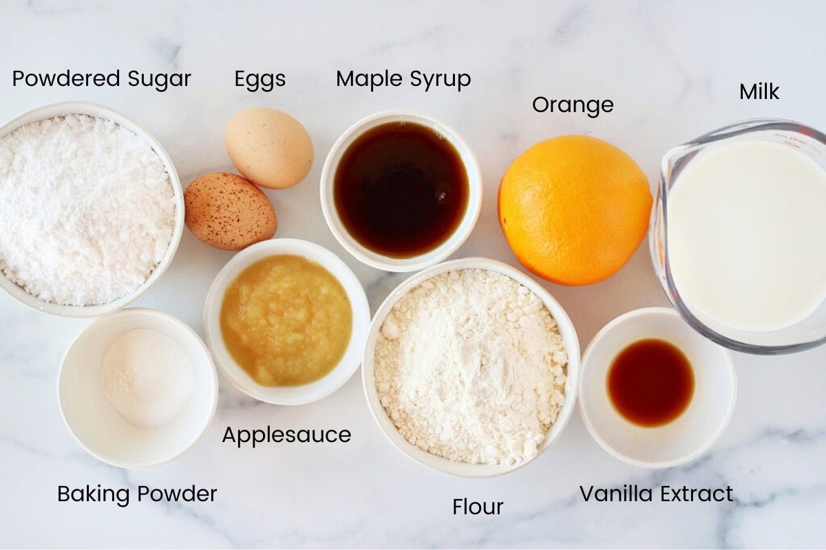 Labeled ingredients for pancake muffins with fresh orange on a white countertop.