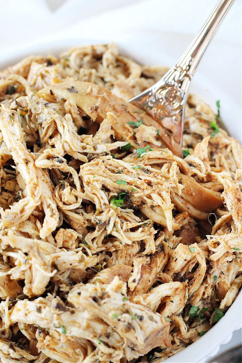 A gold fork in a bowl of zesty crockpot shredded chicken.