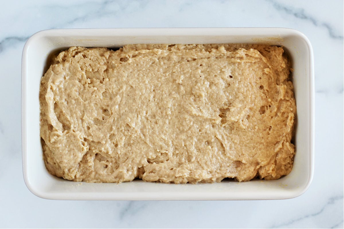 Quick bread batter in a greased metal bread pan on a white marble countertop.