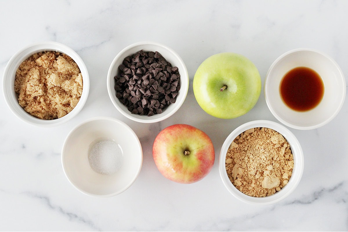 Ingredients for peanut butter caramel apple nachos on a white marble countertop.