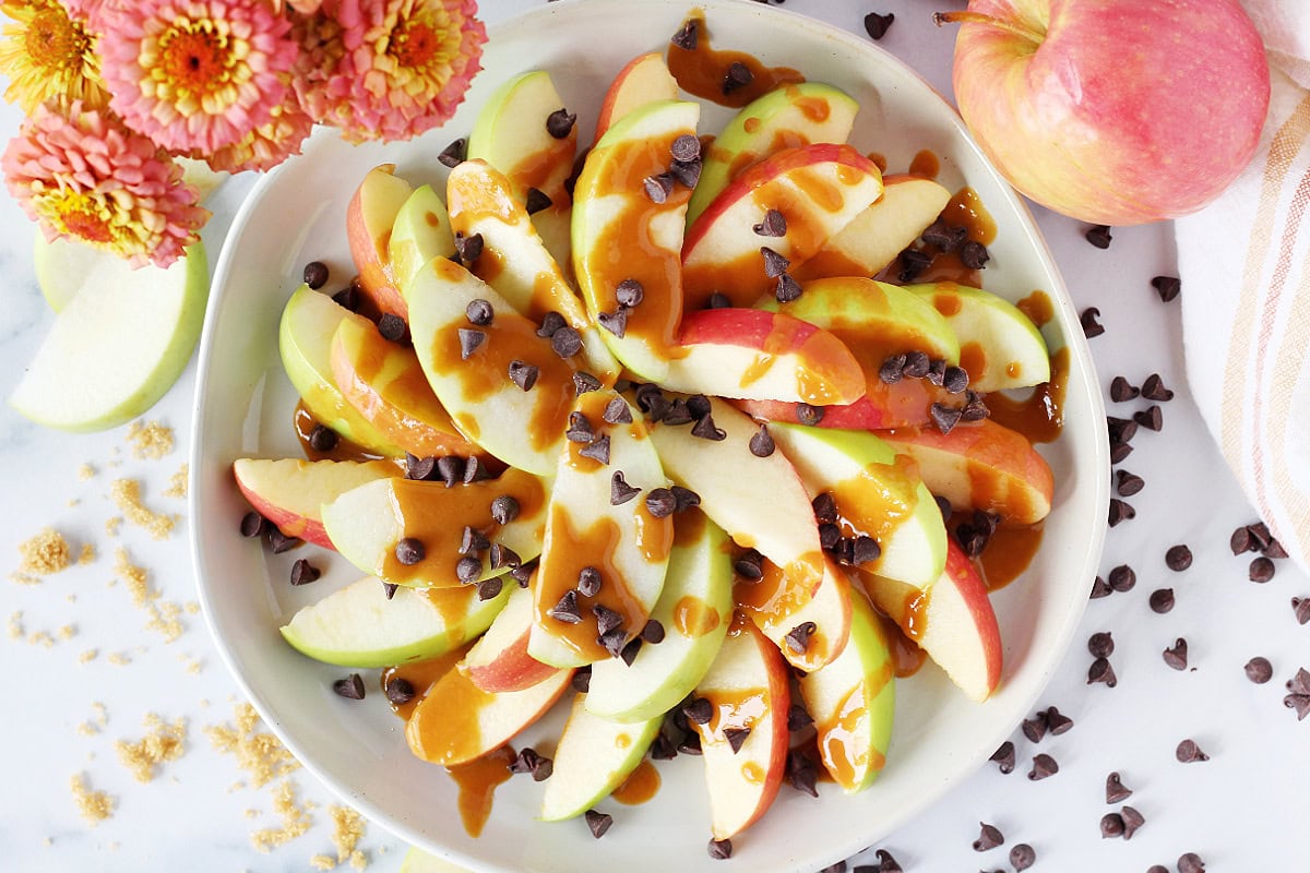 Overhead photo of sliced apples drizzled with a peanut butter caramel sauce and chocolate chips.