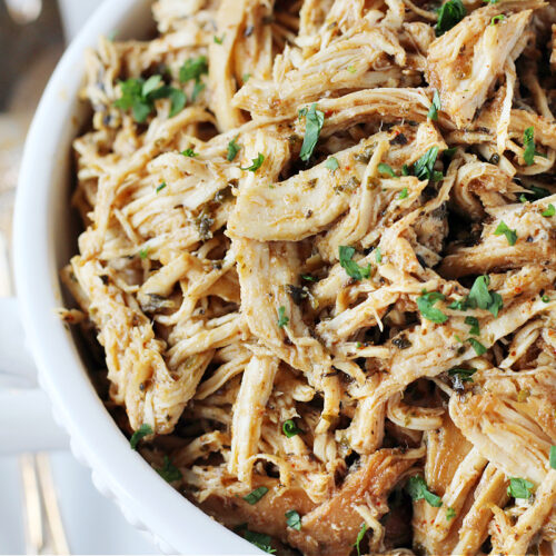 Up close photo of zesty crockpot shredded chicken in a white serving bowl.