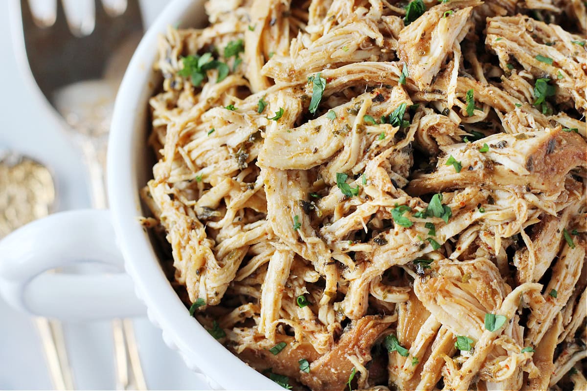 Up close photo of zesty crockpot shredded chicken in a white serving bowl.