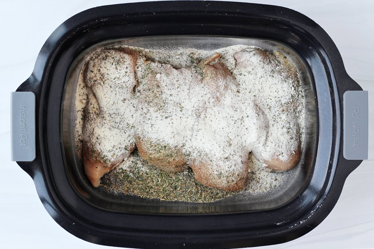 Ranch and Italian seasoning topping four chicken breasts in a crockpot.