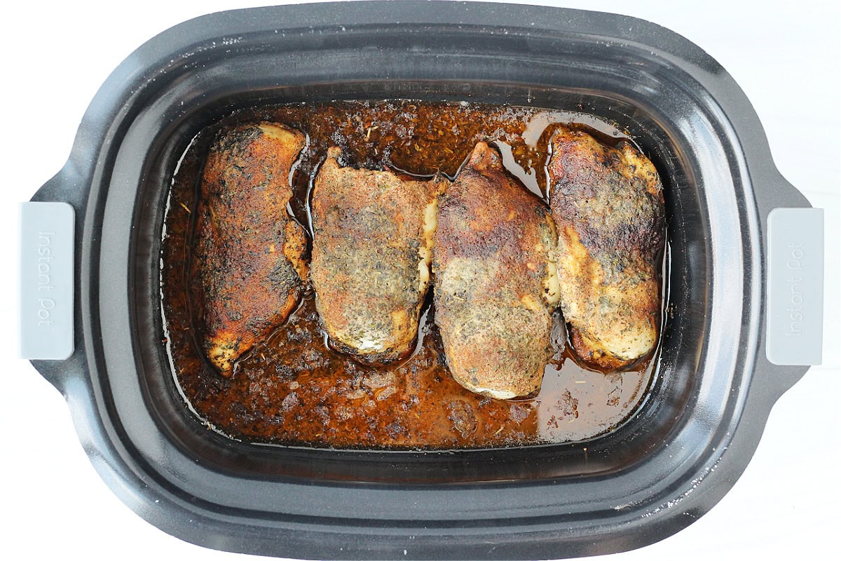 Overhead photo of seasoned and cooked chicken breasts in a slow cooker.