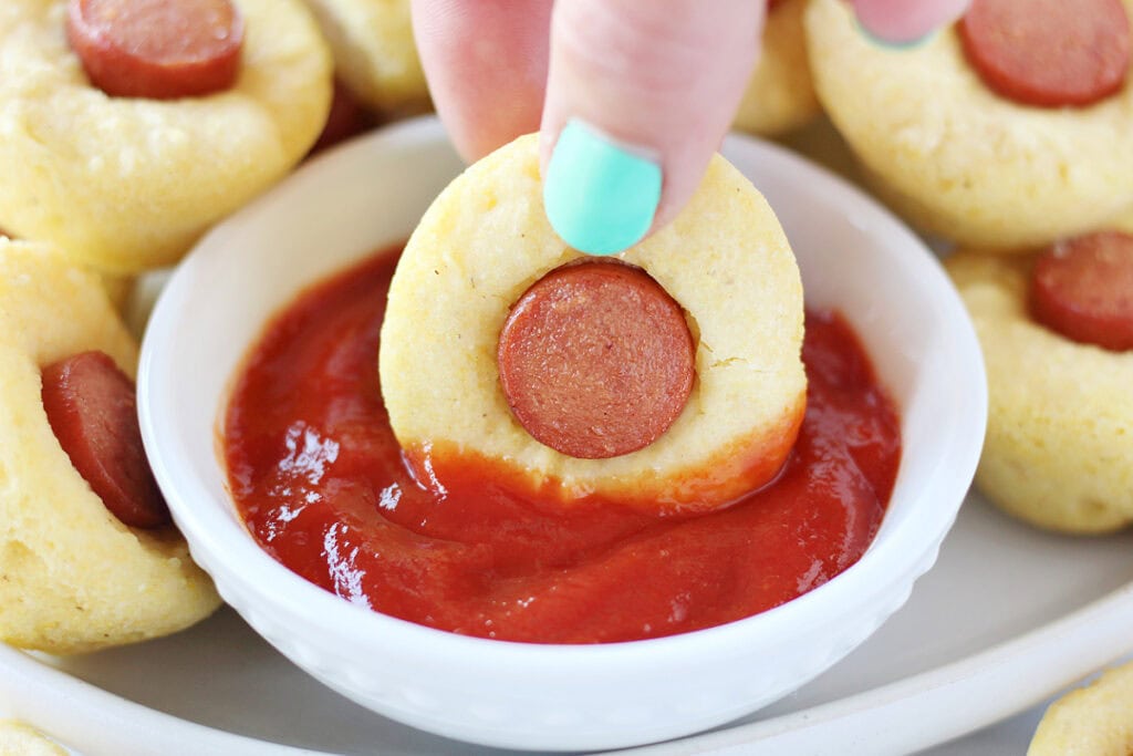 A mini corn dog muffin being dipped in a bowl of ketchup.