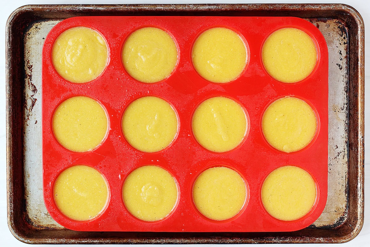 Egg batter in twelve silicone muffin cups on a sheet pan.