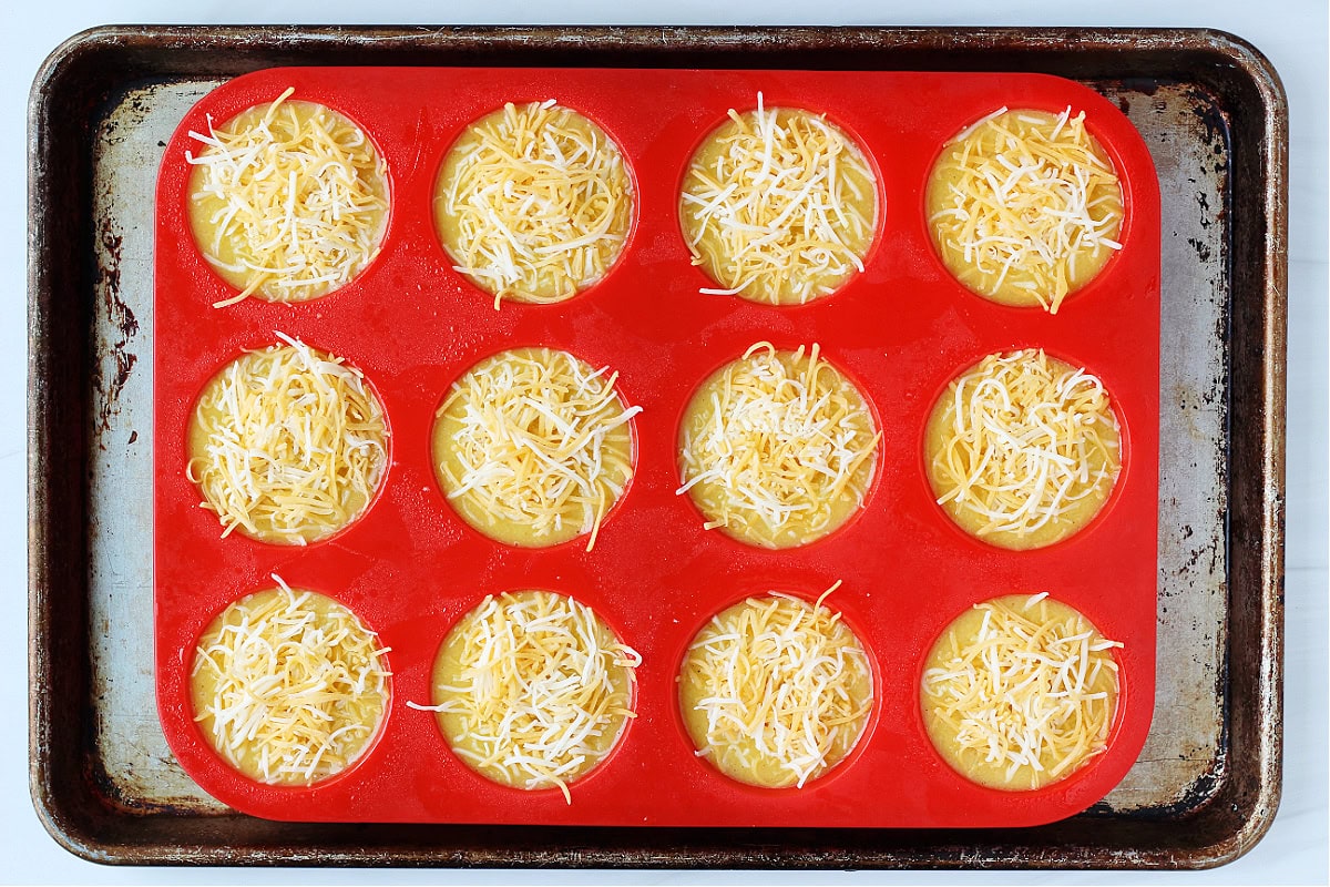 Overhead photo of egg batter topped with cheese in a silicone muffin pan.