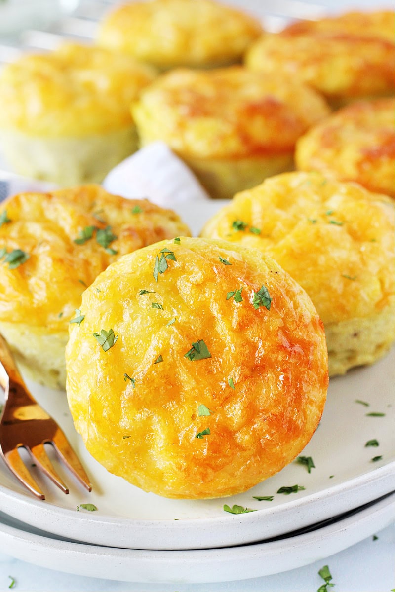 A breakfast egg muffin on a plate with two others topped with fresh parsley.