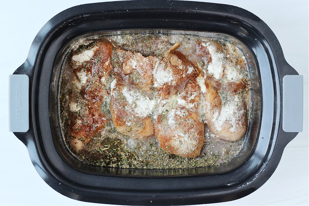 Overhead photo of a crockpot with four chicken breasts topped with seasonings.