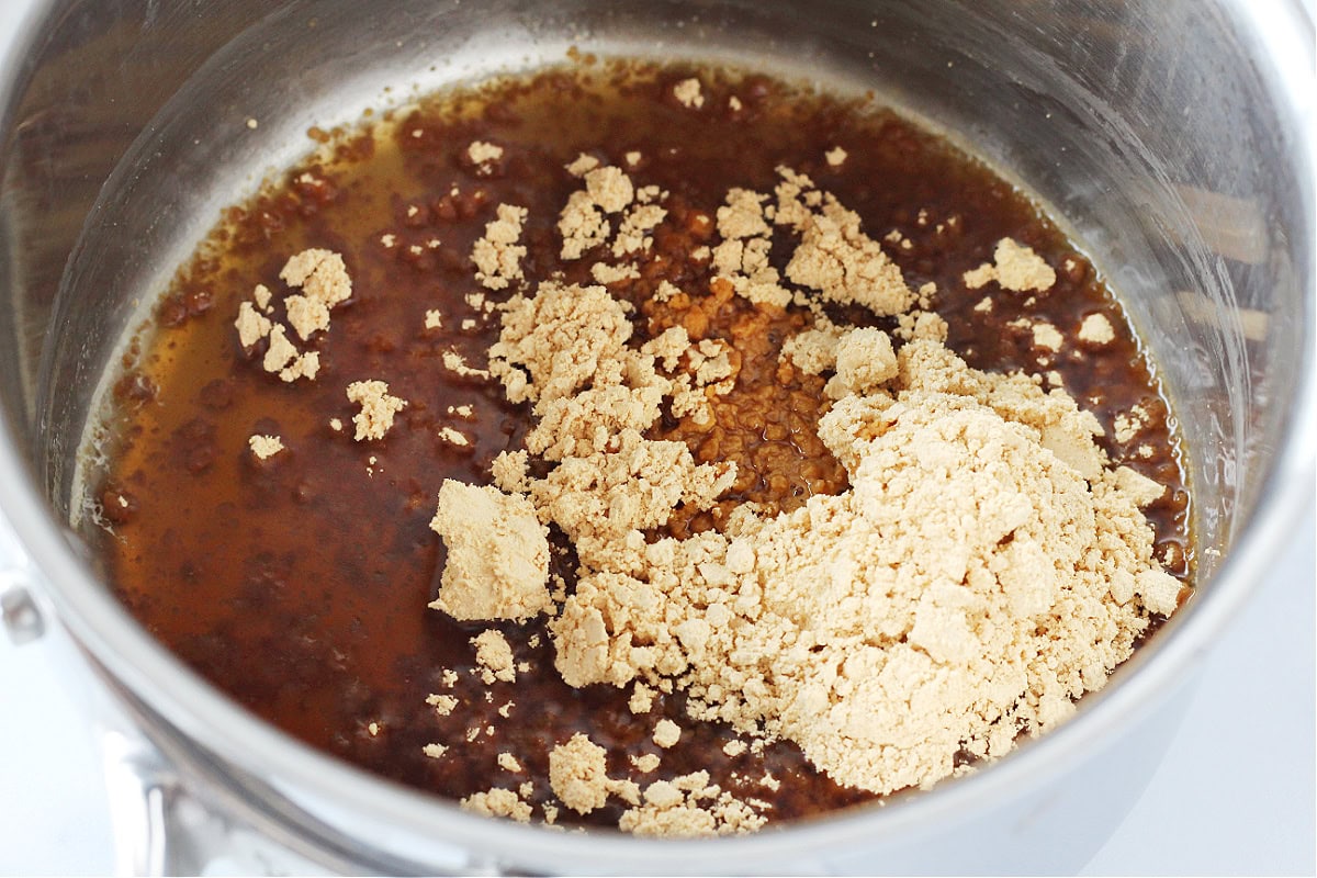 Powdered peanut butter on top of brown sugar syrup in a stainless steel pan.