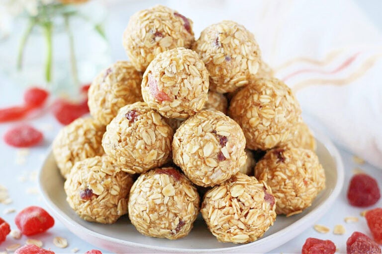 A stack of PB&J energy bites on a white plate surrounded by dried strawberries.