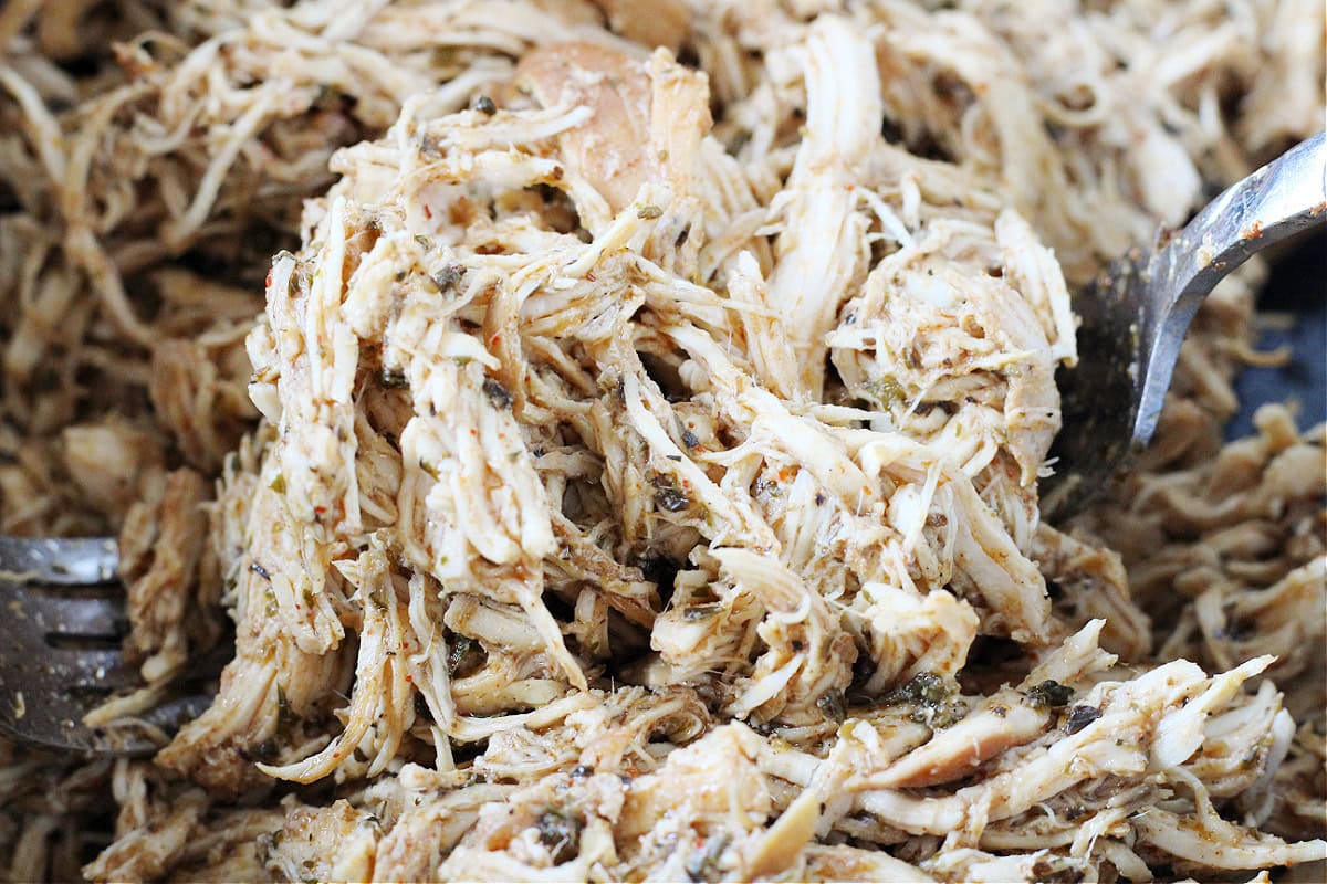 Up close photo of shredded chicken in a flavorful sauce between two forks.