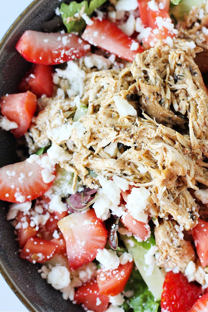 Up close overhead photo of shredded chicken on top of a salad with feta cheese.