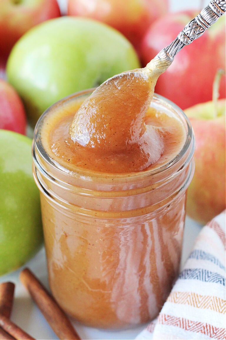 A spoon removing homemade apple butter from a mason jar.