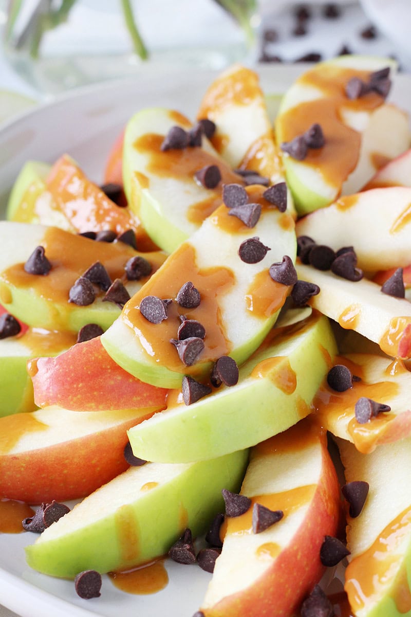 Apple nachos on a plate drizzled with a peanut butter caramel sauce and chocolate chips.