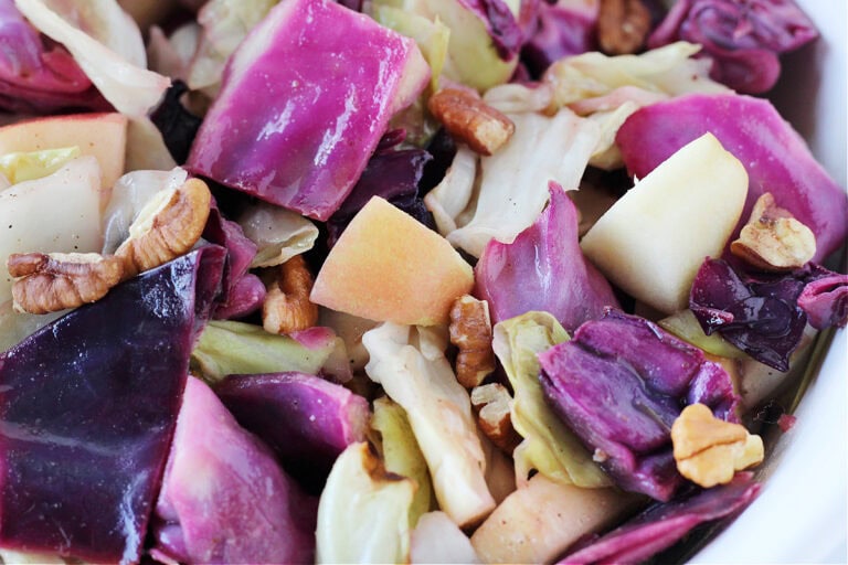 Up close photo of green and purple roasted cabbage and pecans in a bowl.