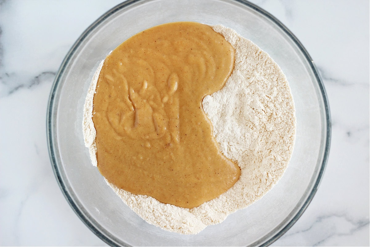 Wet ingredients poured on top of dry ingredients in a glass bowl for quick bread.