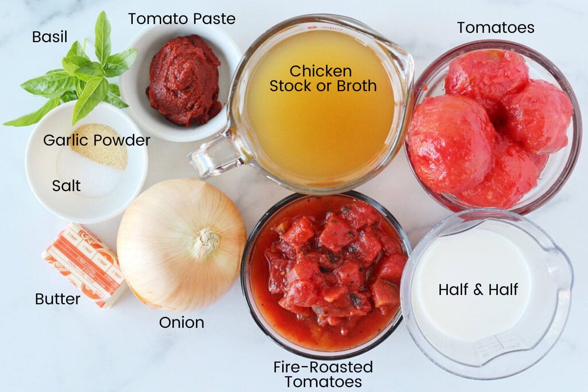 Ingredients for creamy homemade tomato soup with basil on a white marble countertop.