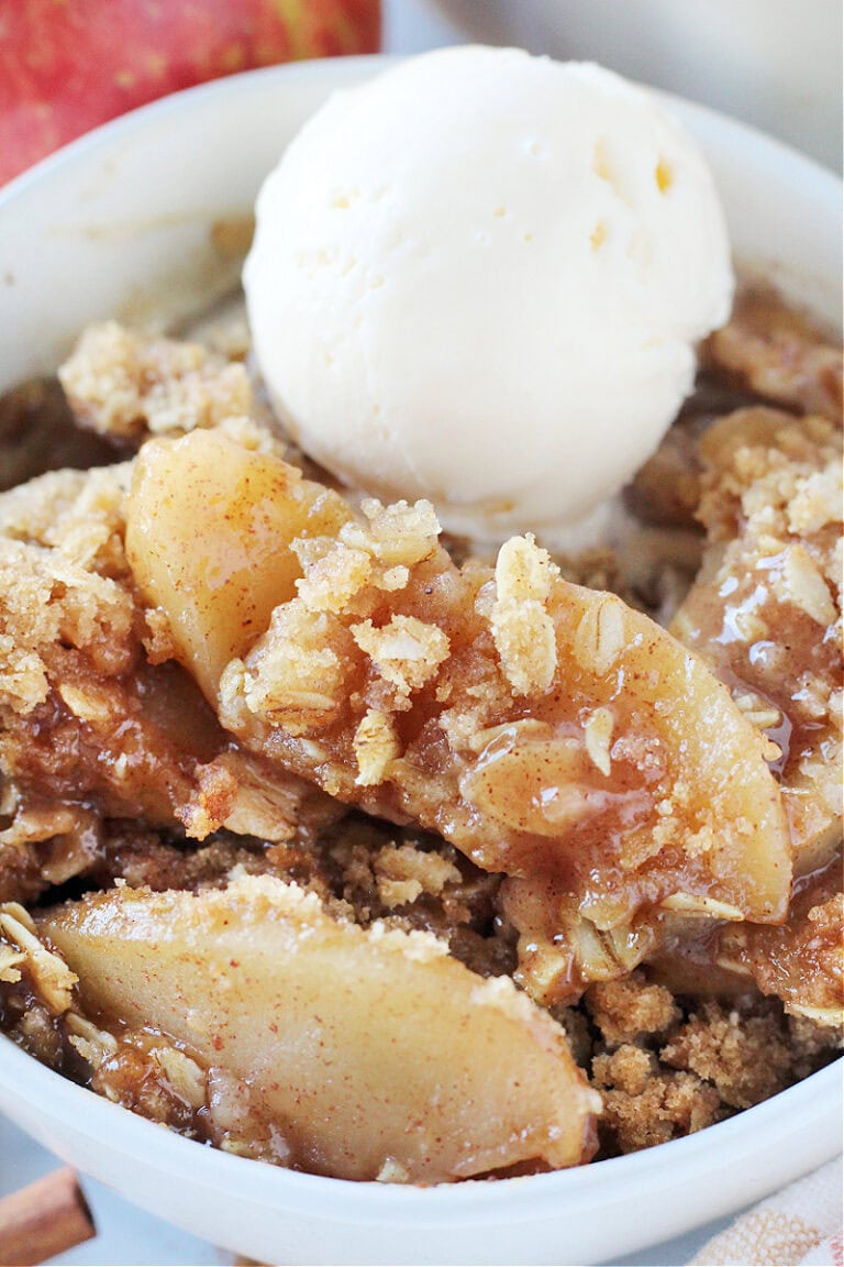 Cinnamon sugar sauce and crumble topping covering apples in a bowl with ice cream.