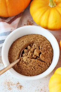 Copper spoon in a bowl of homemade pumpkin spice surrounded by pumpkins.