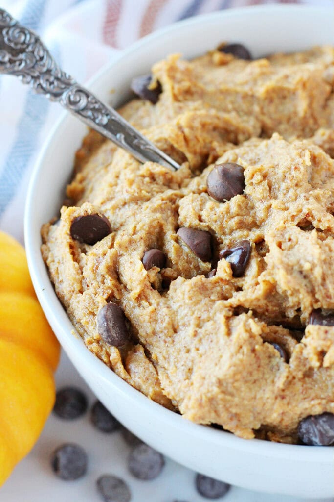 Side view of protein pumpkin cookie dough in a white bowl with spoon.