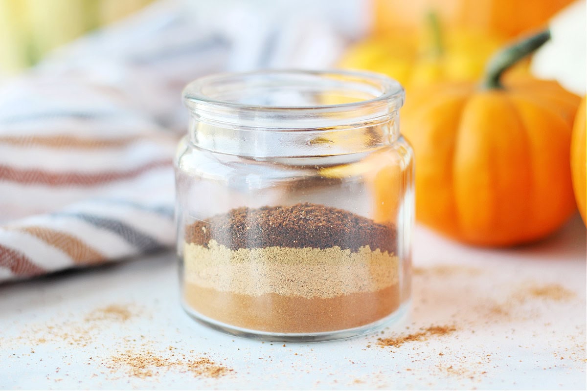 A small glass jar with layers of cinnamon, nutmeg, ginger and cloves.