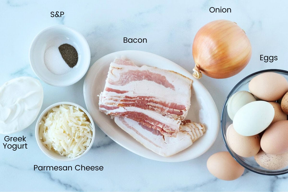 Ingredients for frittata including bacon, onion, and eggs on a white marble countertop.