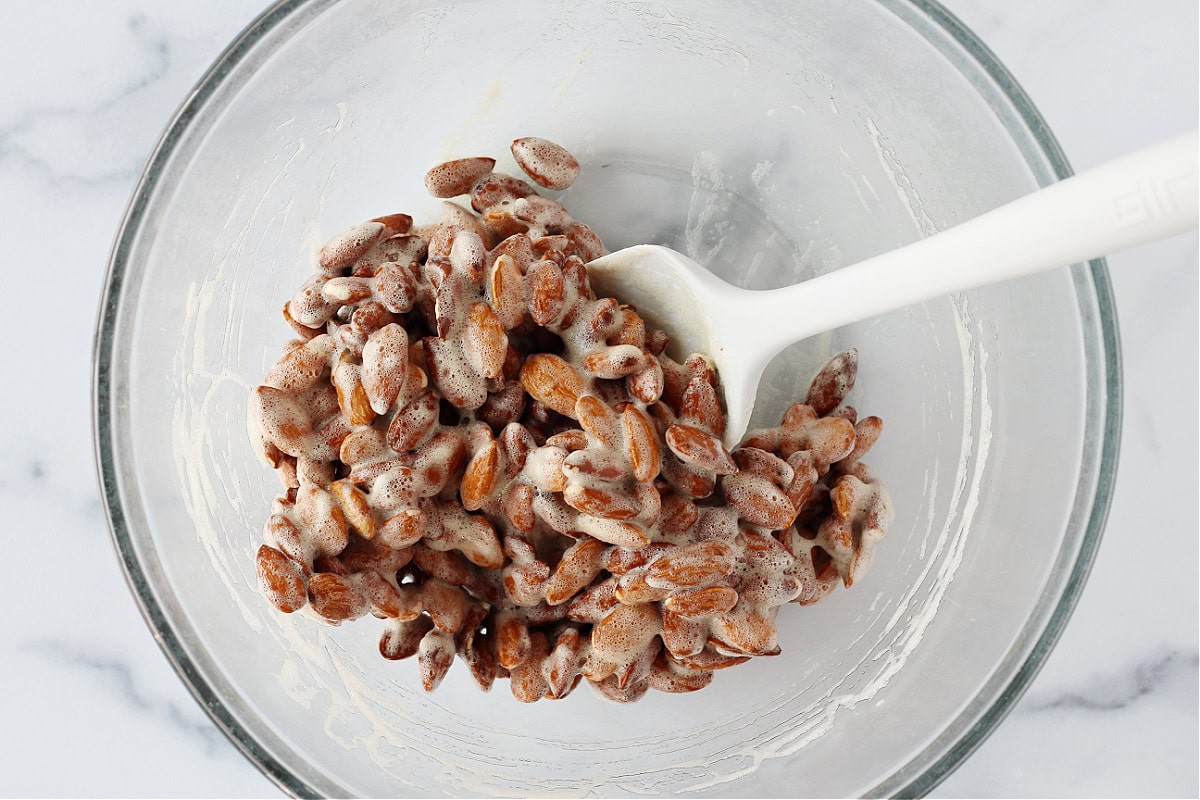 Overhead photo of frothed egg whites covered almonds in a mixing bowl.