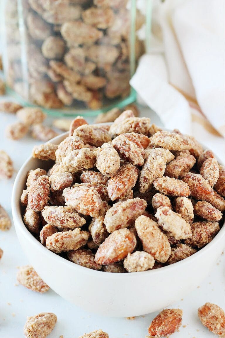 White bowl filled with easy candied almonds with a jar of almonds behind it.