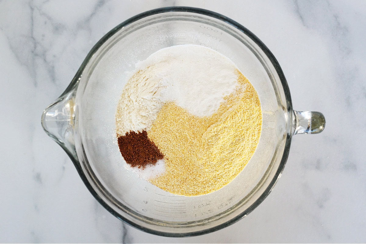 Overhead photo of cornmeal, pumpkin pie spice and flour in a mixing bowl.