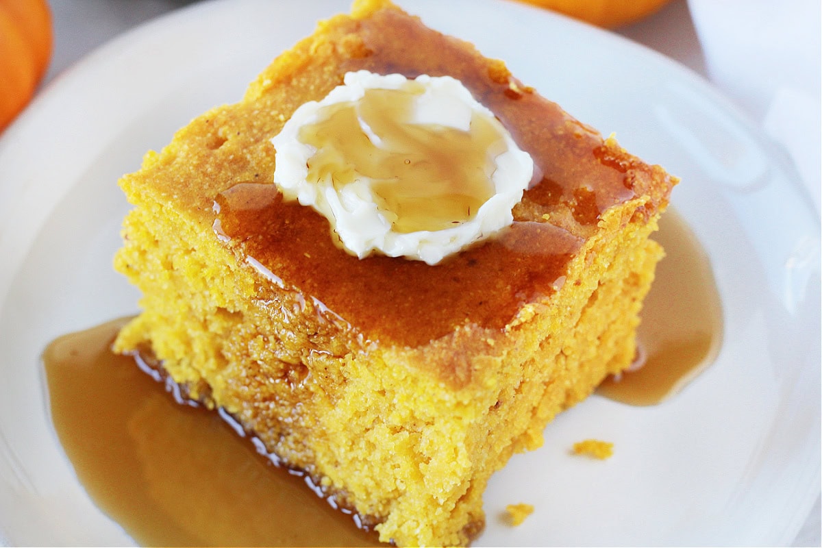 Up close slice of healthy pumpkin cornbread topped with butter and maple syrup.