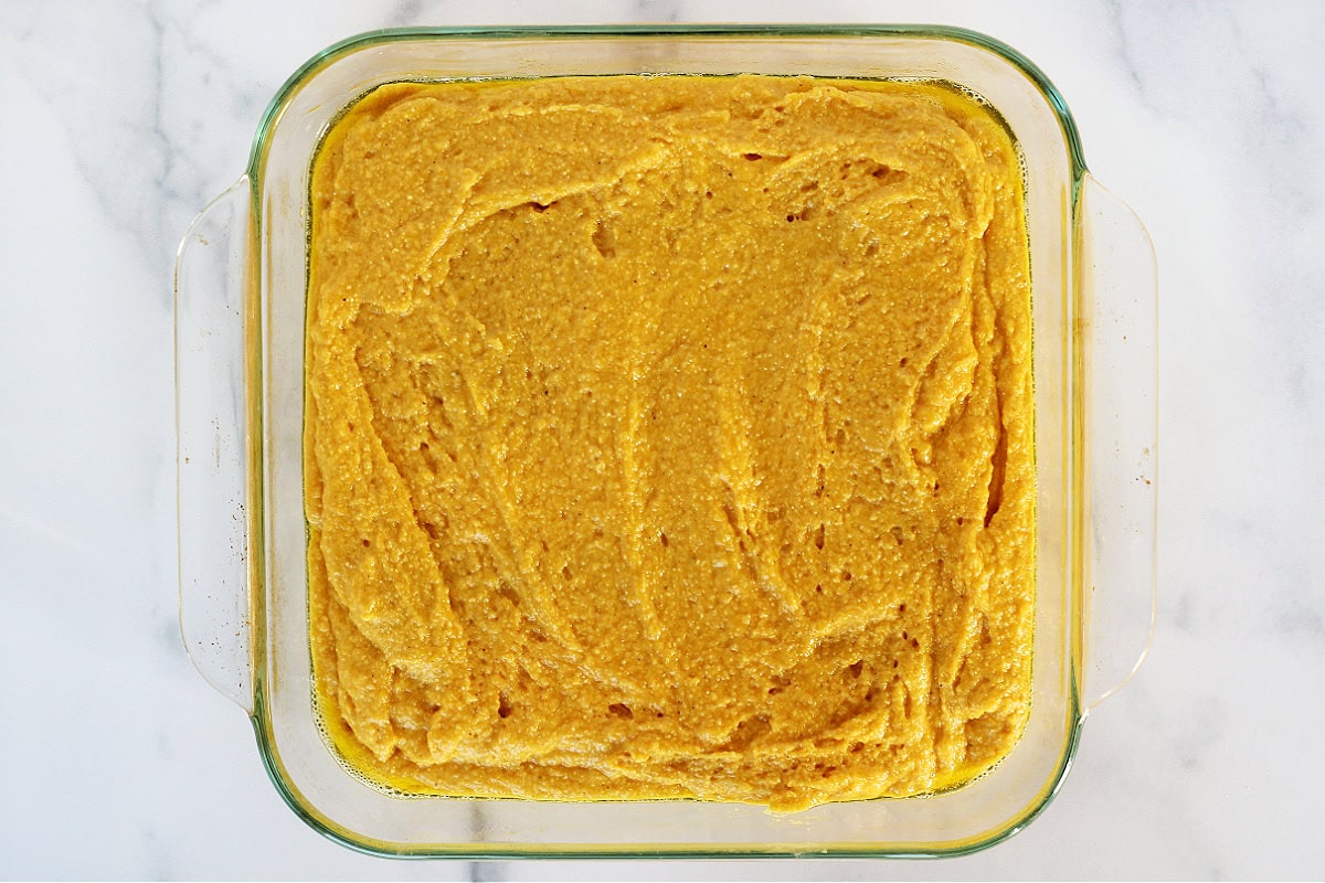 Pumpkin cornbread batter in a glass 8x8 pan.