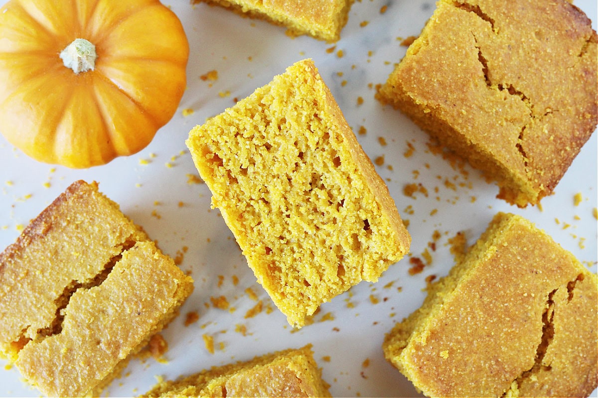 A piece of cornbread on it's side surrounded by other pieces and a pumpkin.