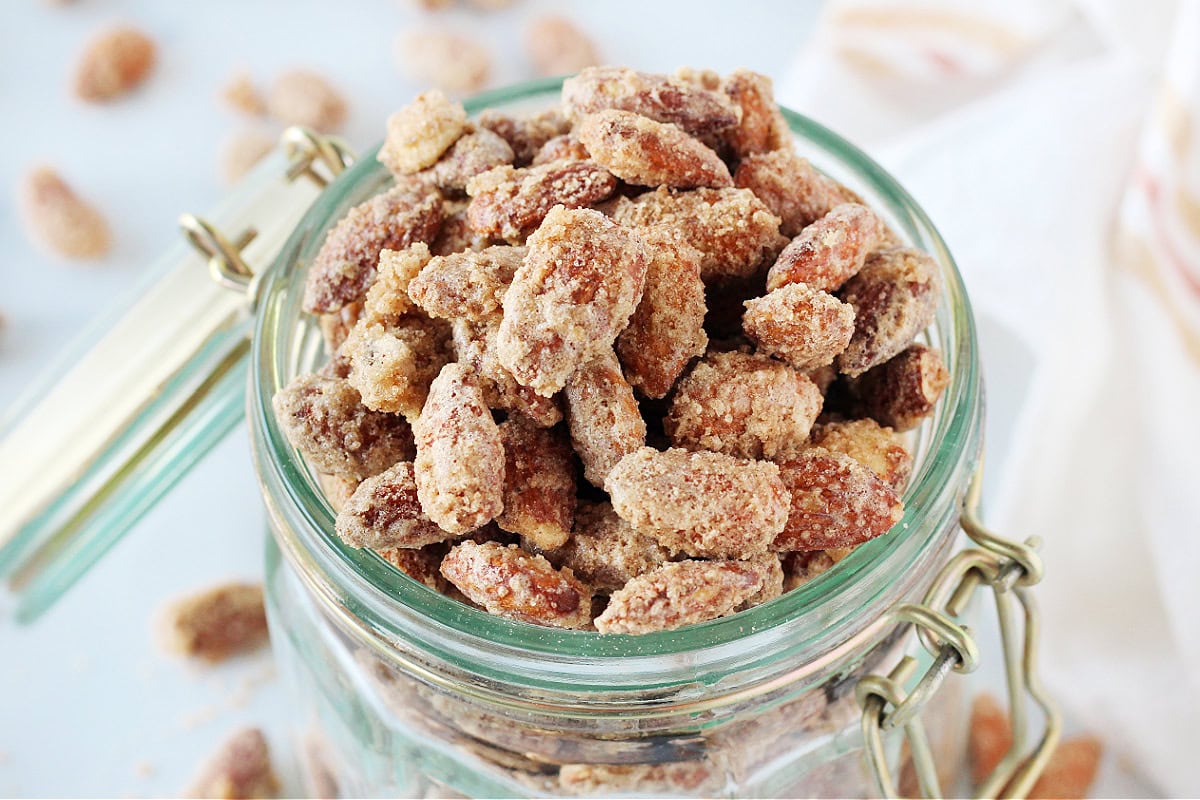 A jar overflowing with baked cinnamon sugar almonds.