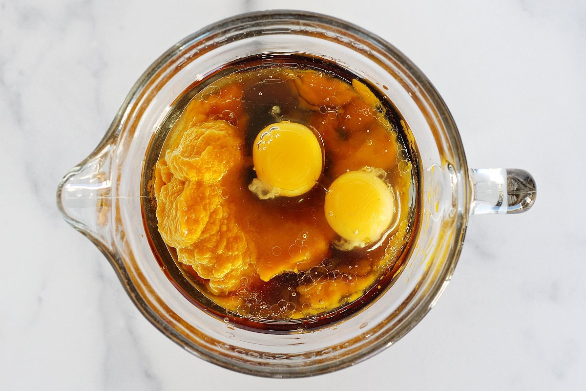 Overhead photo of eggs, pumpkin puree and oil in a glass mixing bowl.