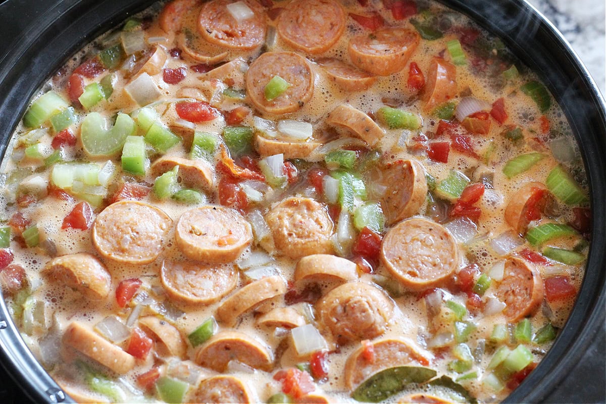 Chicken andouille sausage, vegetables, and broth in a black soup pot.