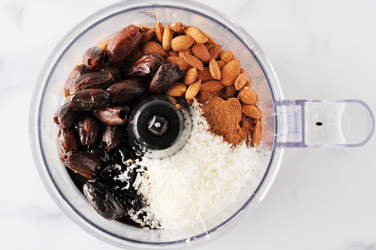 Overhead photo of almonds, dried dates, shredded coconut and molasses in a food processor.