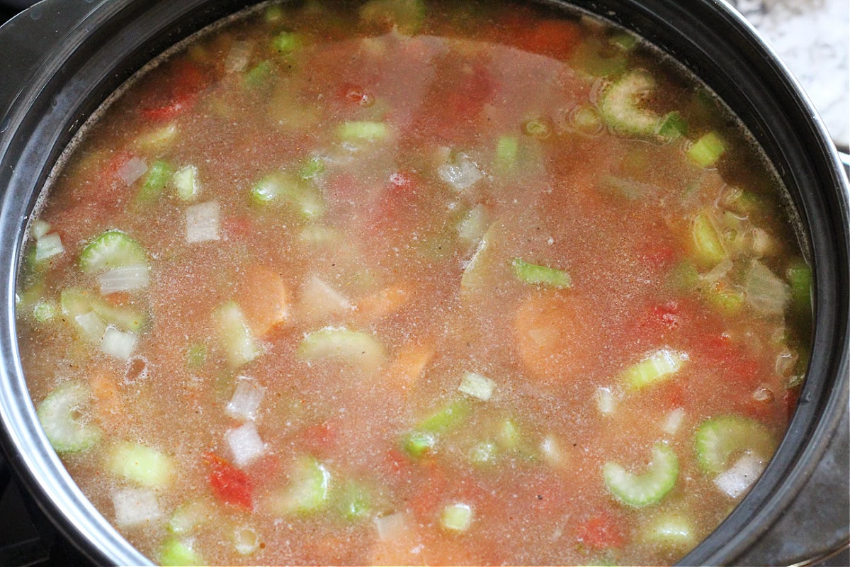 Broth with vegetables in a black soup pot.