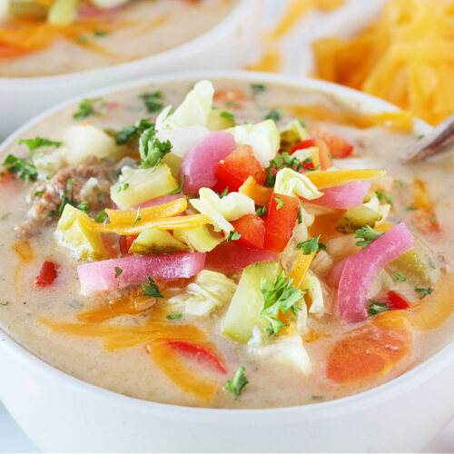 Up close photo of cheeseburger soup topped with shredded cheese, lettuce, pickles and parsley.