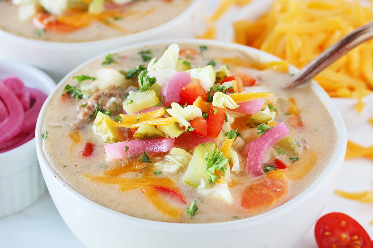 Up close photo of cheeseburger soup topped with shredded cheese, lettuce, pickles and parsley.