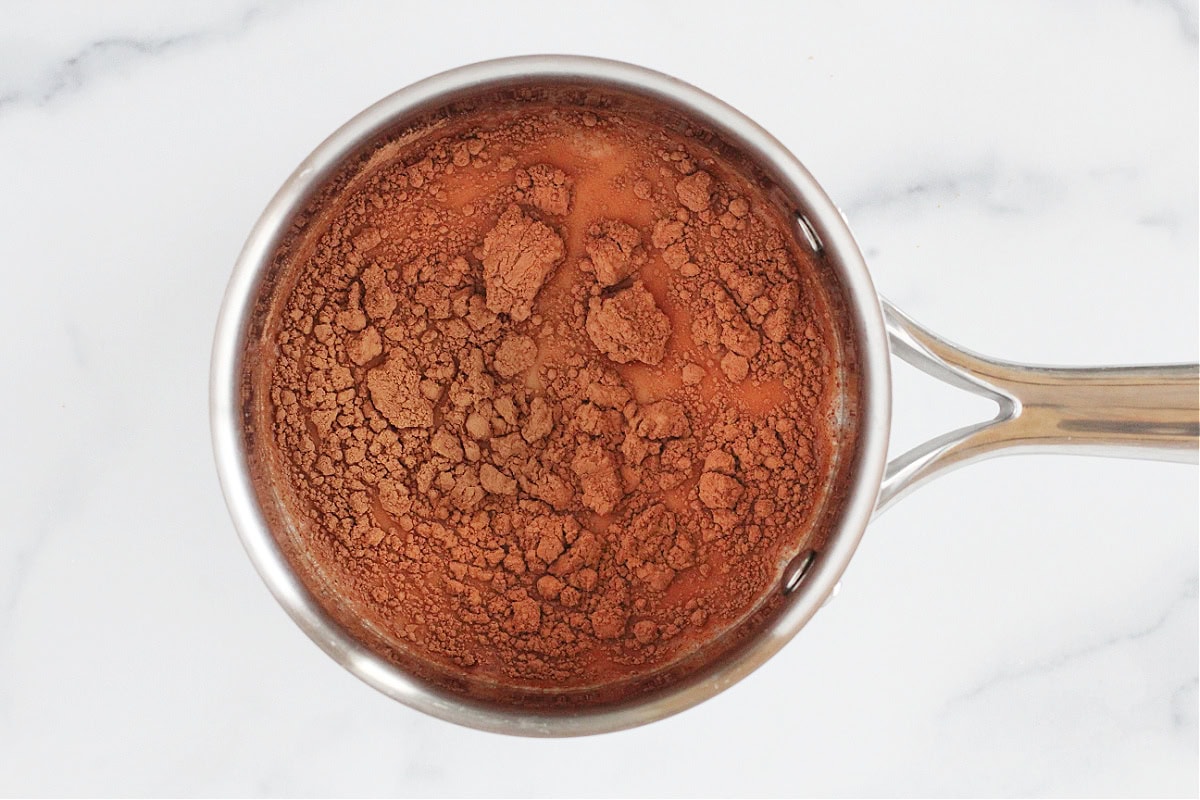 Cocoa powder on top of milk in a small soup pot.