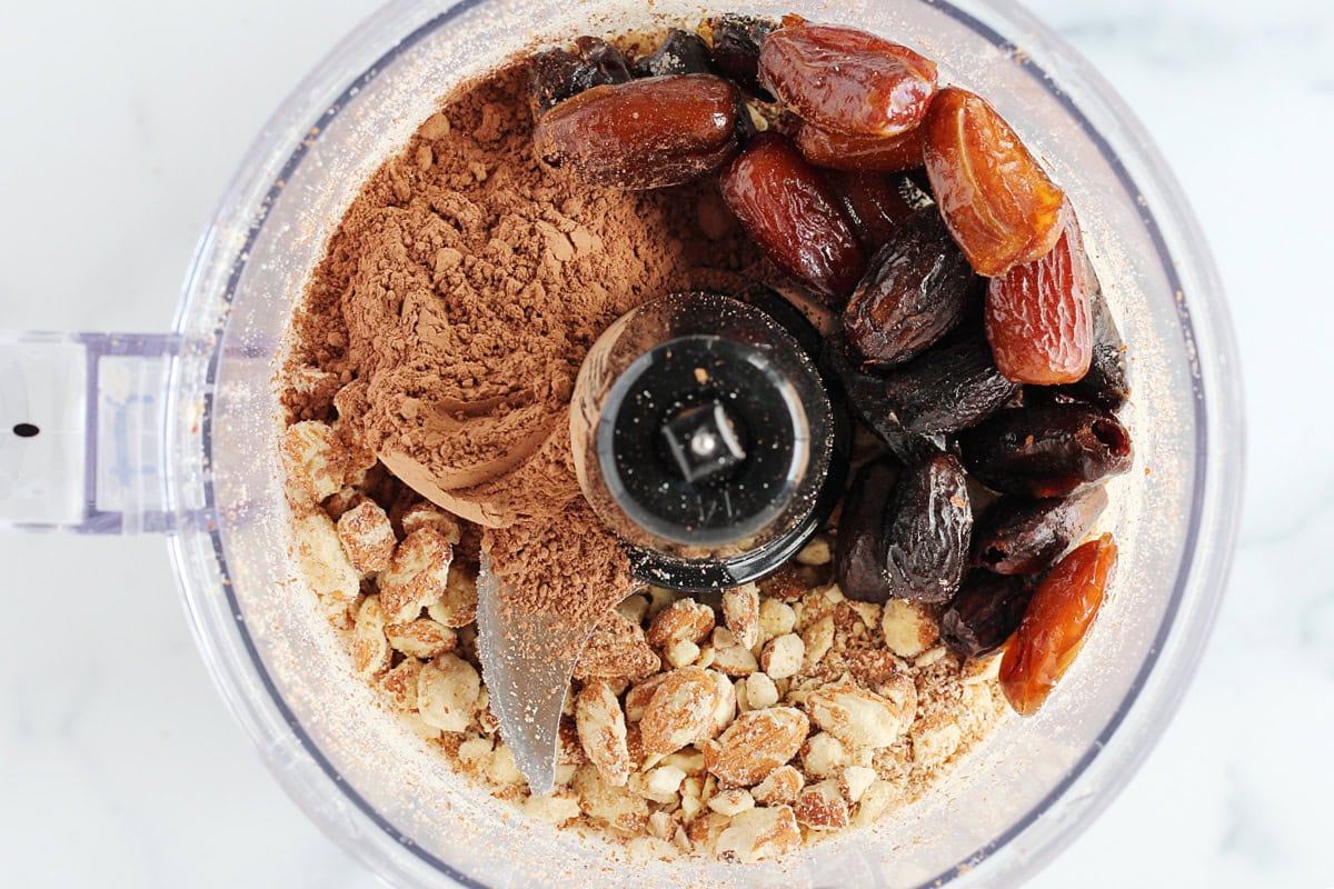 Dried dates, cocoa powder, and almonds in the bowl of a food processor.