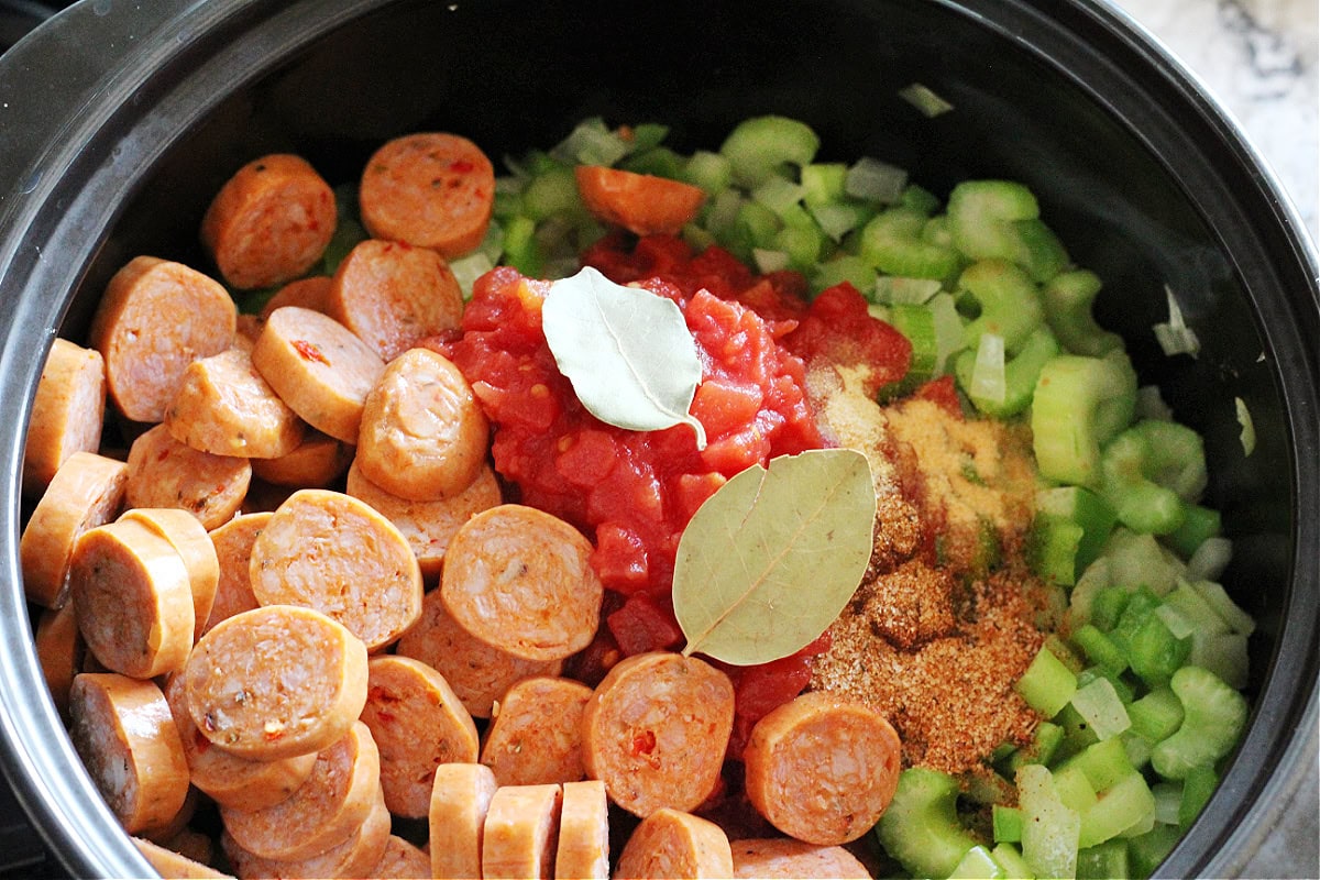 Bay leaves, chicken andouille sausage, the holy trinity, and diced tomatoes in a soup pot.