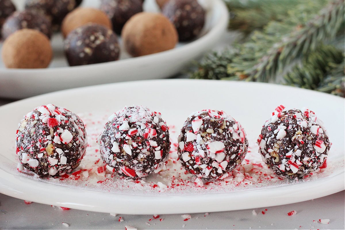 Four no bake chocolate mint balls on a white plate covered in crushed candy canes.